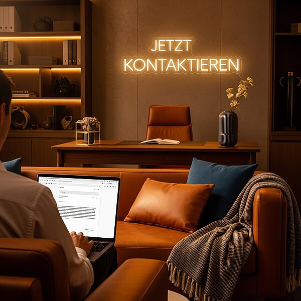 Mann im Ledersessel mit Laptop auf dem Schoß, an der Wand Neoschrift: jetzt kontaktieren